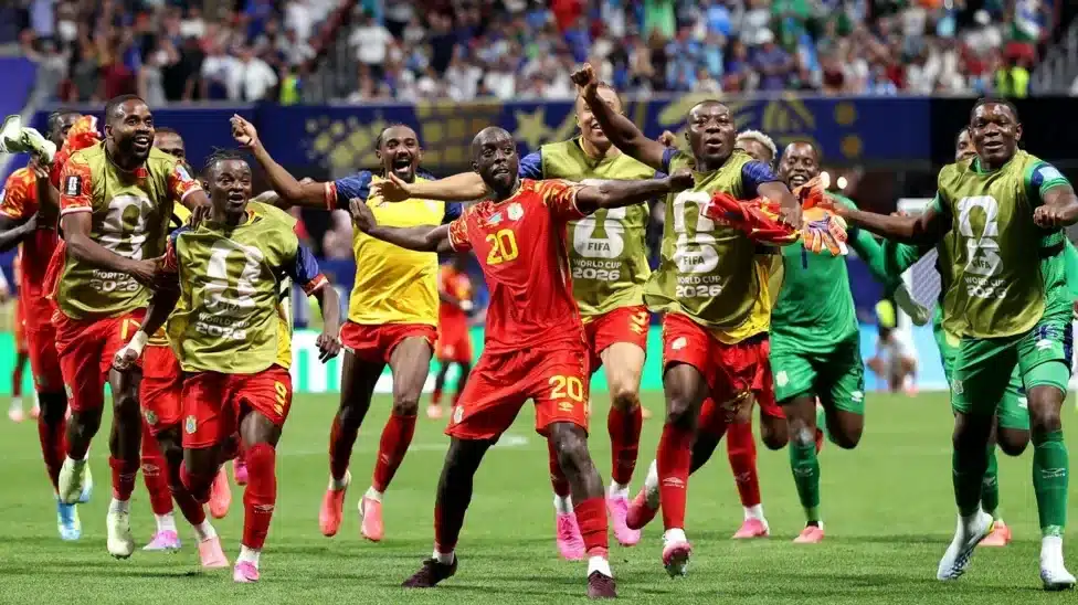Yoane Wissa spreads his arms out as he dances in celebration after scoring a goal against Uzbekistan and the World Cup finals. He is surrounded by several DR Congo substitutes, who all bear smiles as some of them copy his pose
