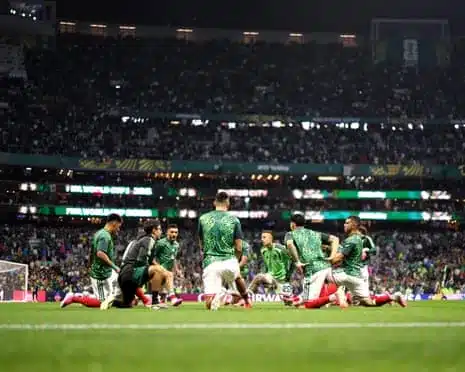 Mexico players in green patterned jerseys stretch and warm up on a pitch in a packed stadium