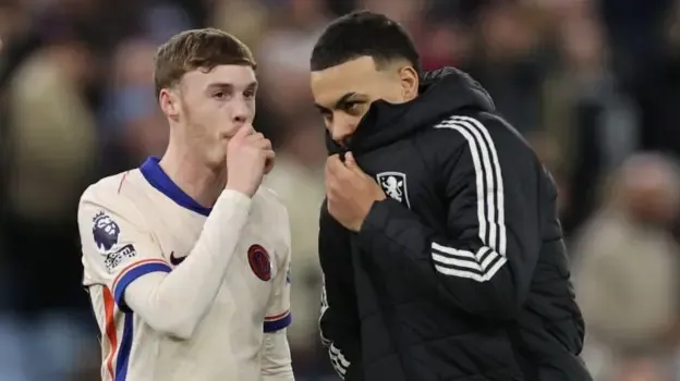 Cole Palmer and Morgan Rogers hiding their mouths while speaking to each other after a match